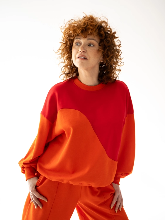 Bluza Terra Sun oversize w kolorze czerwono-pomarańczowym z asymetrycznym, geometrycznym cięciem na przodzie.