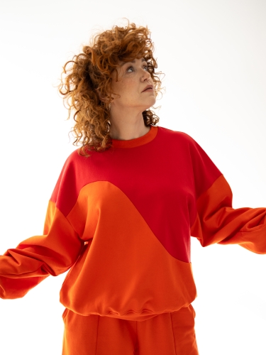 Bluza Terra Sun oversize w kolorze czerwono-pomarańczowym z asymetrycznym, geometrycznym cięciem na przodzie.