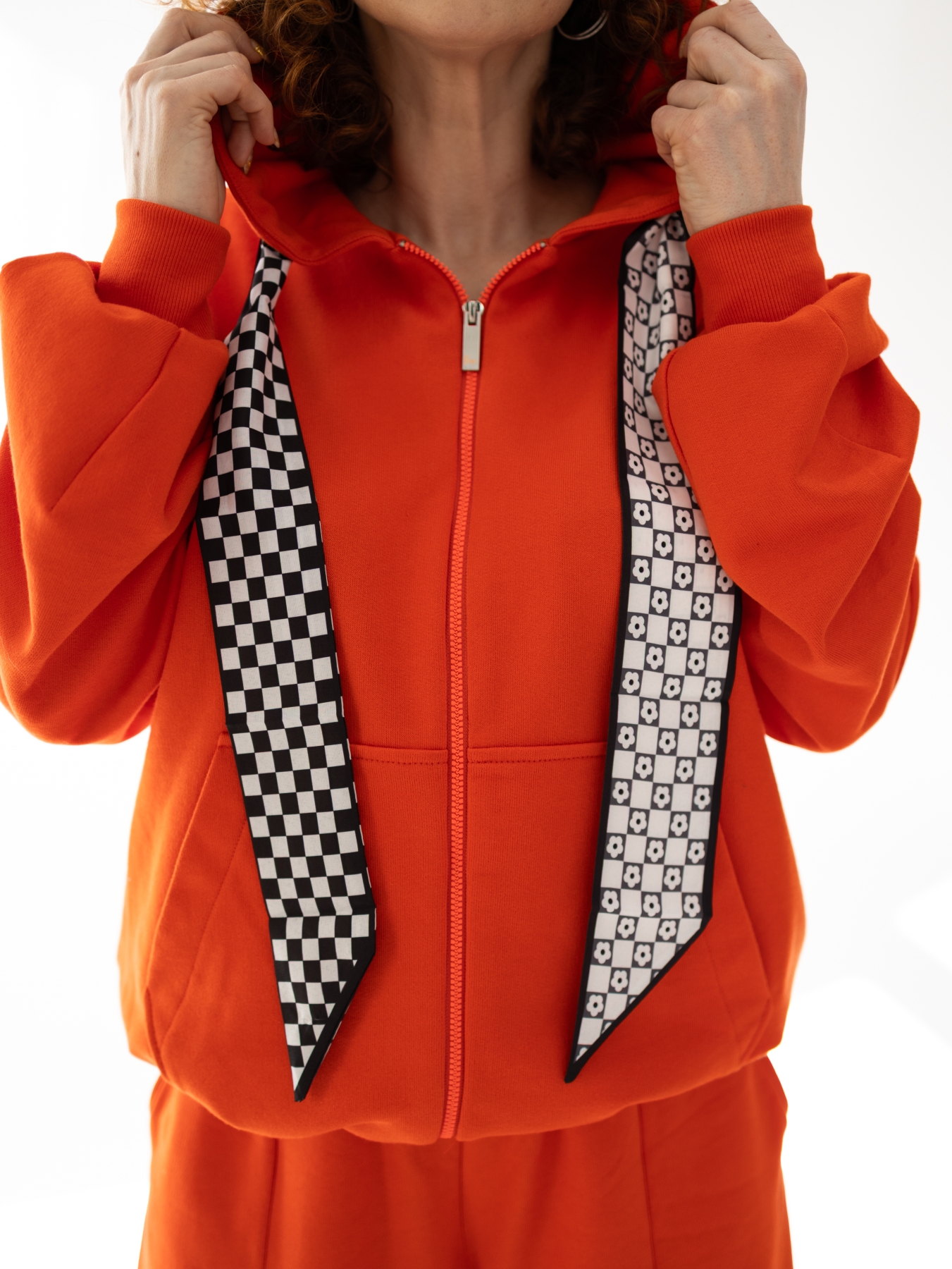 Pomarańczowa bluza Rosella z kapturem, suwakiem i ozdobnymi troczkami w czarno-białe wzory.