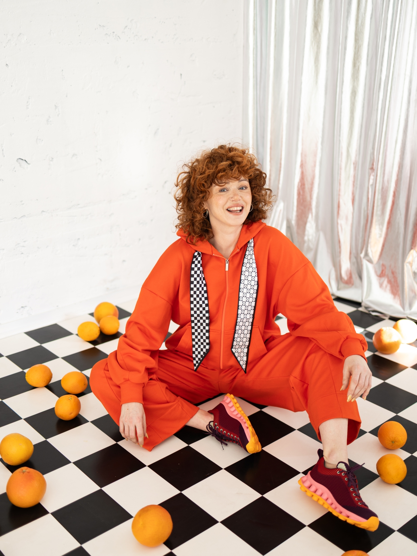 Pomarańczowa bluza Rosella z kapturem, suwakiem i ozdobnymi troczkami w czarno-białe wzory.