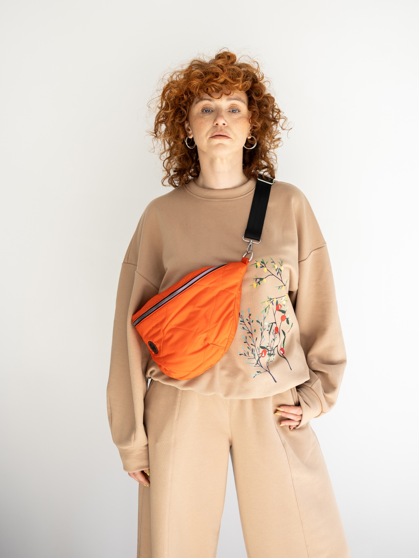 Beżowa bluza oversize z długim rękawem i subtelnym roślinnym printem z przodu, zestawiona z beżowymi spodniami. Modelka stoi przy jasnej ścianie.