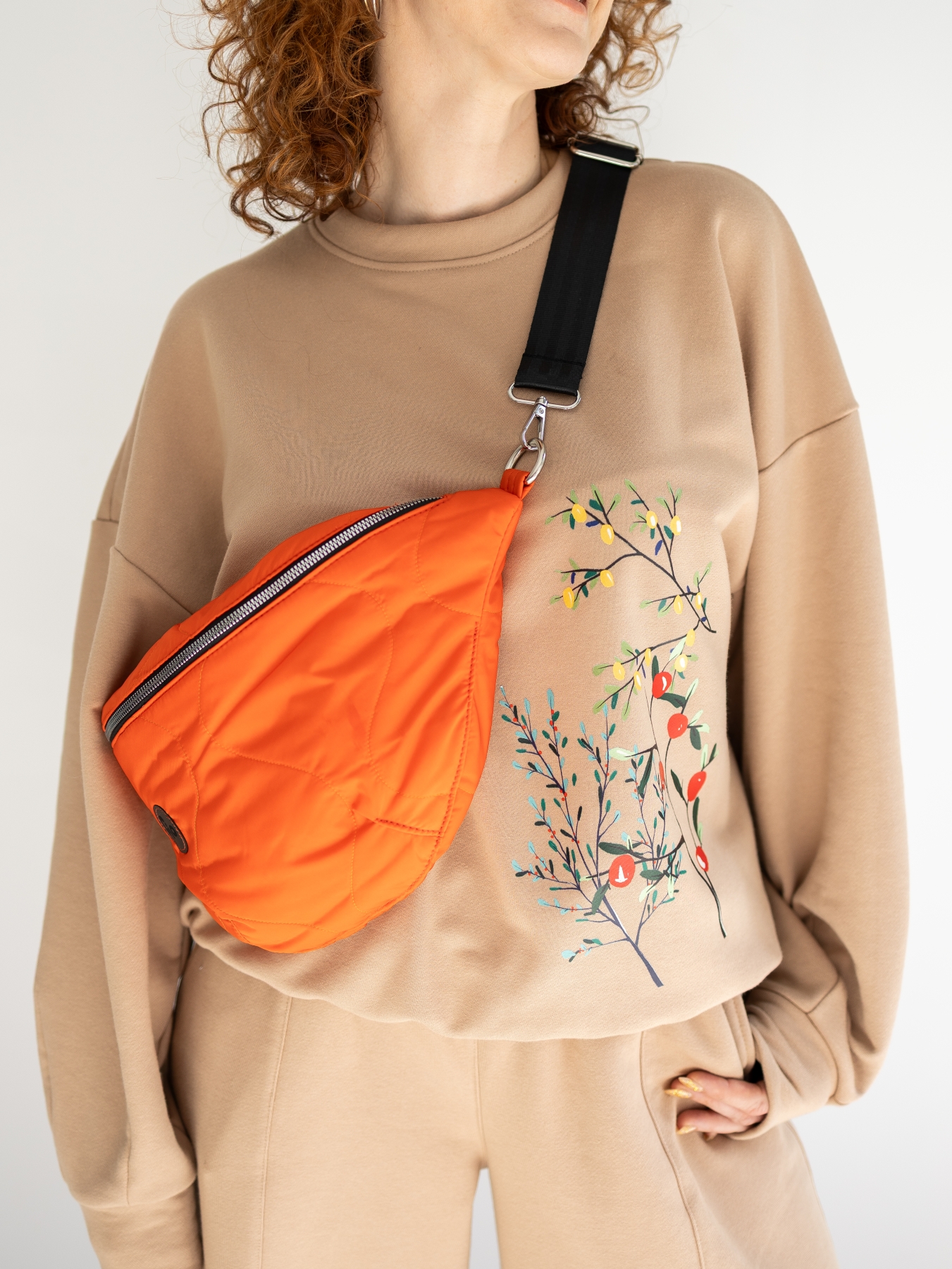 Beżowa bluza oversize z długim rękawem i subtelnym roślinnym printem z przodu, zestawiona z beżowymi spodniami. Modelka stoi przy jasnej ścianie.