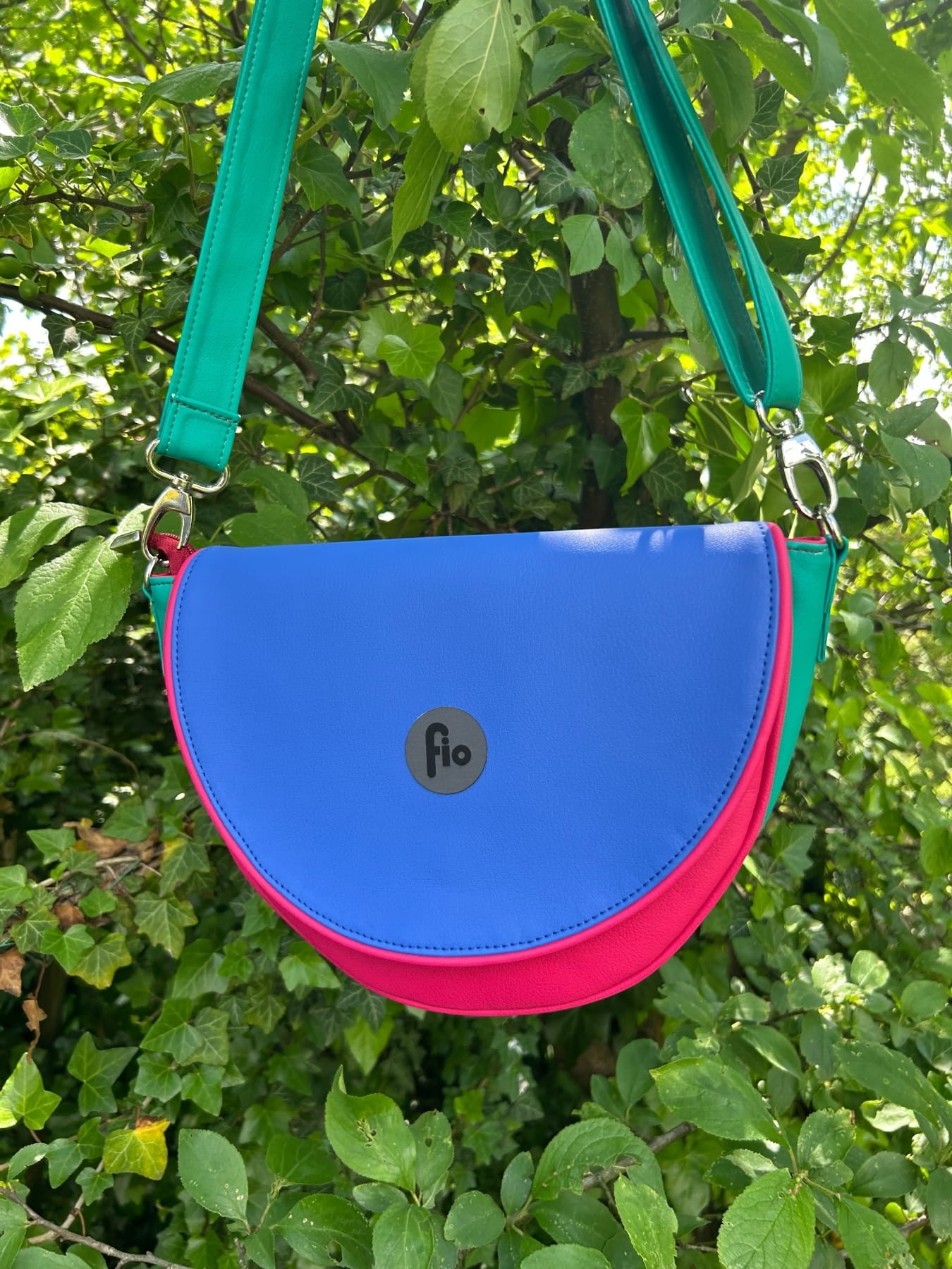 Nerka półokrągła zawieszona na zielonym pasku, z niebieską klapką i różowym przodem.